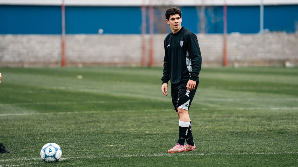 A young soccer player in sports attire stands on a green field during a training session.