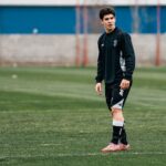 A young soccer player in sports attire stands on a green field during a training session.