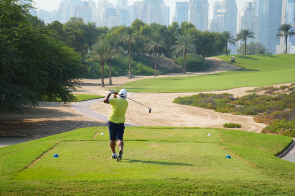 A golfer teeing off on a sunny day with the iconic Dubai skyline in the backdrop.