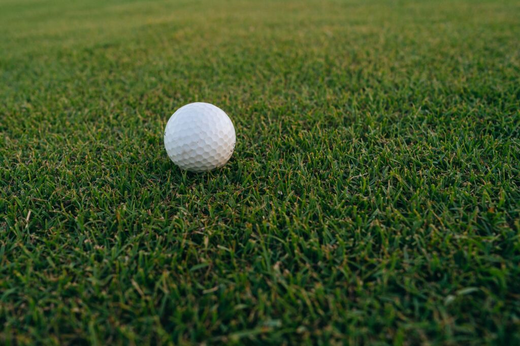 A close-up image of a golf ball resting on vibrant green grass, perfect for sports and recreation themes.