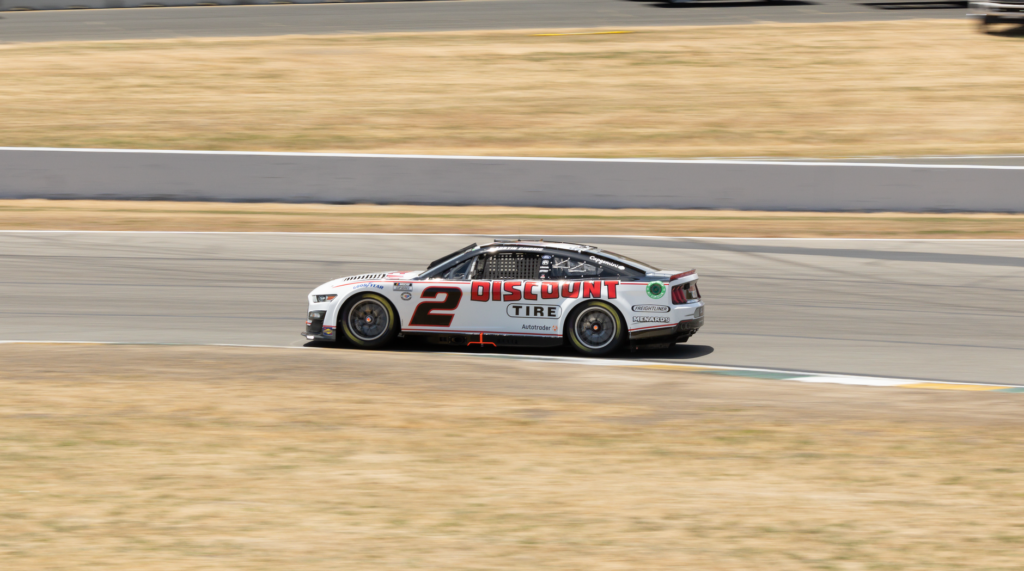 A sports car speeds around a race track during a daytime motorsport event.