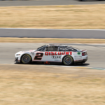 A sports car speeds around a race track during a daytime motorsport event.