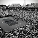 A black and white photo capturing a thrilling tennis match in a crowded outdoor stadium.