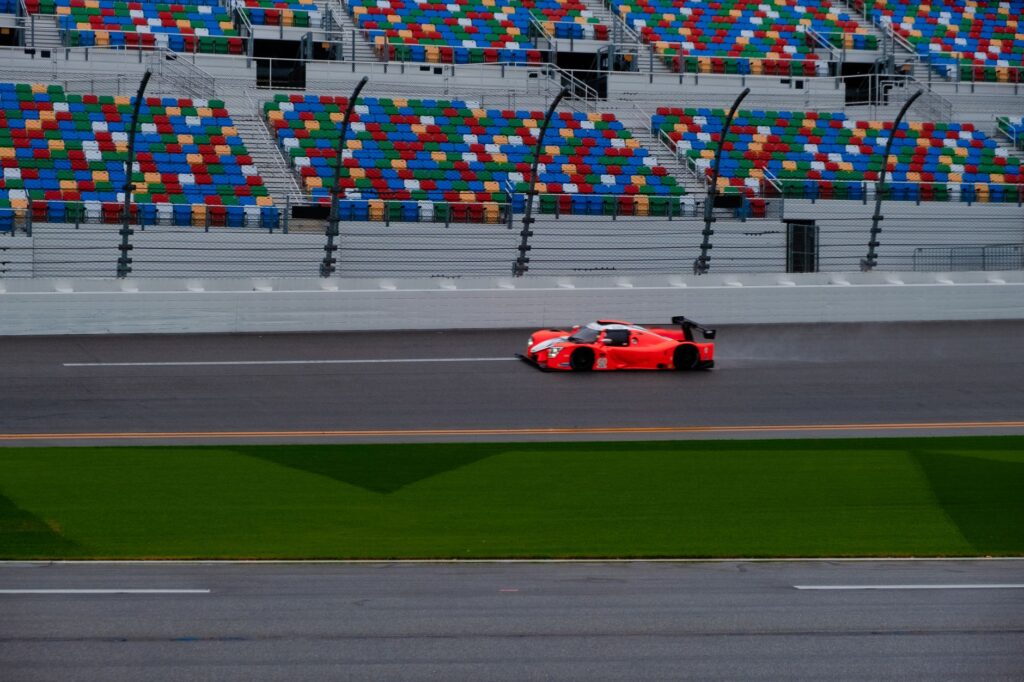 A vibrant red race car speeding on a track with empty colorful stands in the background.