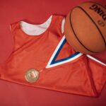 A red basketball jersey paired with a medal and Spalding basketball on a red backdrop.