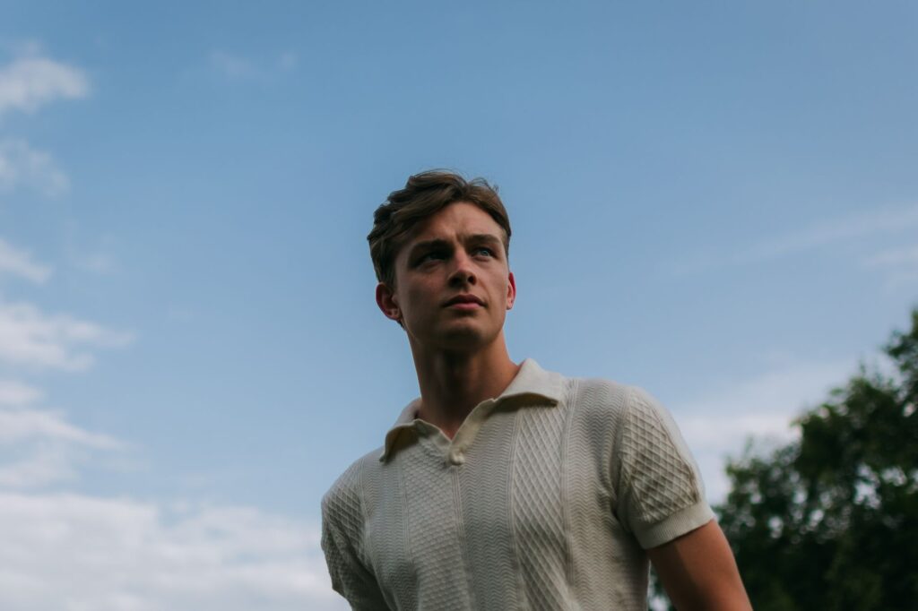 Portrait of a young man outdoors, with a blue sky background, exuding confidence and style.