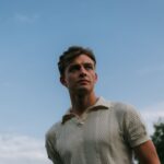 Portrait of a young man outdoors, with a blue sky background, exuding confidence and style.
