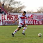 A football player in action on the field during an outdoor match with spectators in the background.