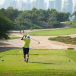 A golfer teeing off on a sunny day with the iconic Dubai skyline in the backdrop.