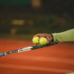 Two people exchanging tennis balls on a clay court during nighttime, focusing on the sport's dynamics.