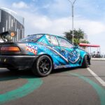 A colorful racing car with decals parked on a city street under a clear sky.