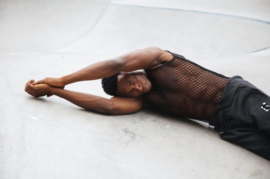 Muscular man in a stylish mesh outfit lying on a concrete background, showcasing strength and style.