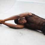 Muscular man in a stylish mesh outfit lying on a concrete background, showcasing strength and style.