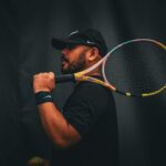 Portrait of a focused male tennis player holding a racket against a dark background.