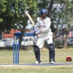 Batsman poised to strike in a cricket match, set outdoors on a sunny day.