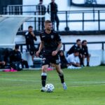 Soccer player dribbling during a match with team watching from the sidelines.