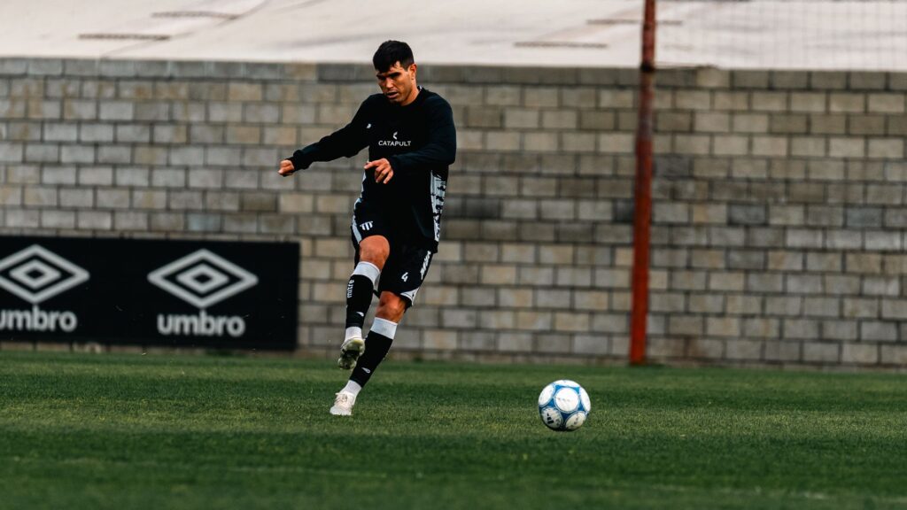 A young male soccer player practicing on a grass field, focusing on a precise kick.