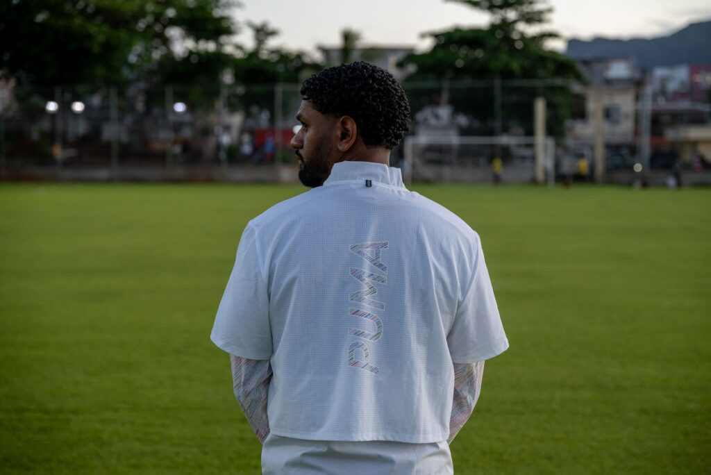 Man wearing a sports jersey stands thoughtfully on a grass field.