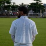 Man wearing a sports jersey stands thoughtfully on a grass field.