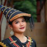 A woman in traditional attire with a decorated hat poses confidently.