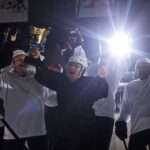 A joyful hockey team celebrates victory holding the trophy on the ice rink.