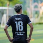 Back view of a soccer player wearing jersey number 18 on a sunny day outdoors.