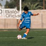 Young soccer player in blue uniform kicking a ball during a match on a sunny day.