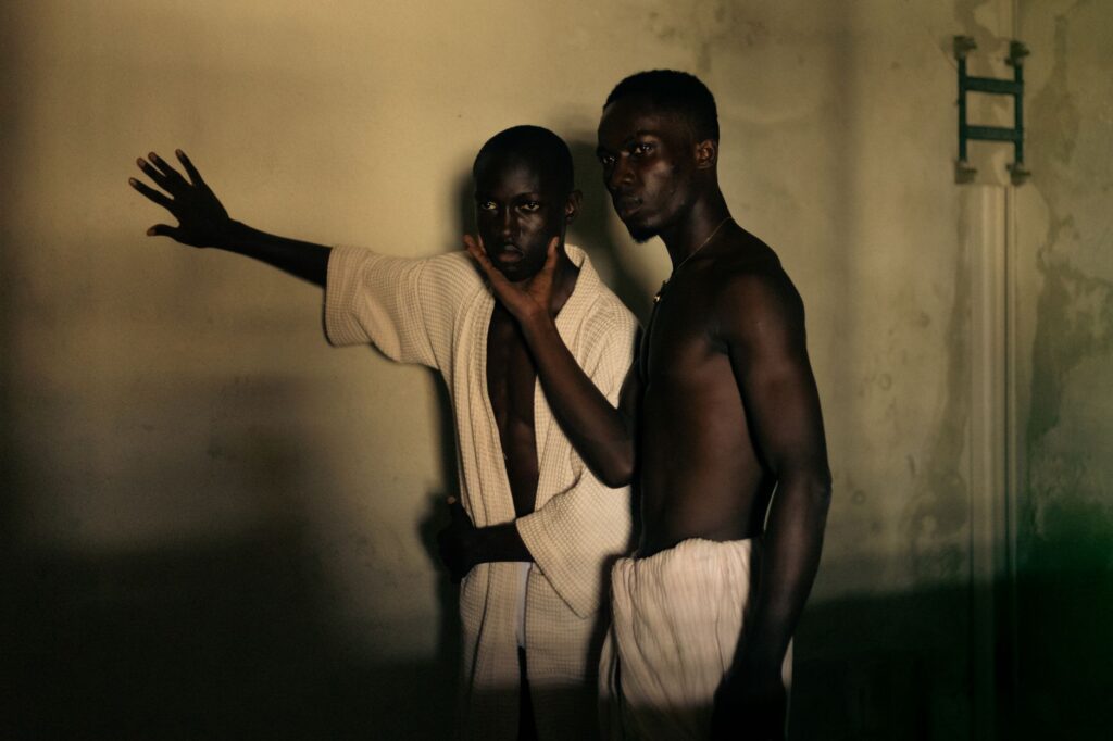 Two men in expressive poses captured in warm, dramatic lighting indoors.