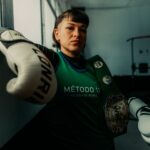 Female boxer in an Argentine gym with championship belt, exuding confidence and strength.