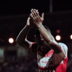 Madura United football player applauding fans during a night game in Bangkalan.