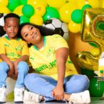 Mother and child in yellow jerseys pose with soccer-themed birthday decorations for a fifth celebration.