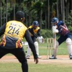Dynamic cricket match scene with batsman, wicketkeeper, and fielder in action.