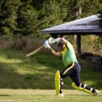 Cricketer batting during a match on a bright sunny day on a green field.