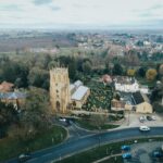 Explore a tranquil aerial view of a historic church and surrounding village, capturing the essence of rural architecture.