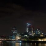 Dramatic night view of London's skyline featuring modern skyscrapers and the historical Tower of London.