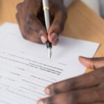 Close-up of a man's hands signing a formal document indoors.