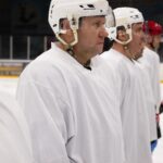 Ice hockey players in white uniforms line up on the rink, ready for action.