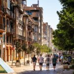 A bustling European street with pedestrians and classic architecture under the summer sun.