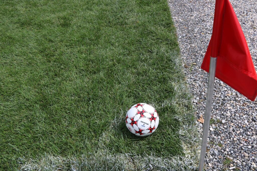 A close-up of a soccer ball near a red corner flag on a grass field, ideal for sports themes.