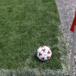 A close-up of a soccer ball near a red corner flag on a grass field, ideal for sports themes.
