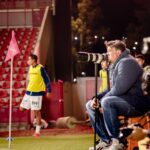 Soccer coach intensely watches game at night stadium, focused on strategy.