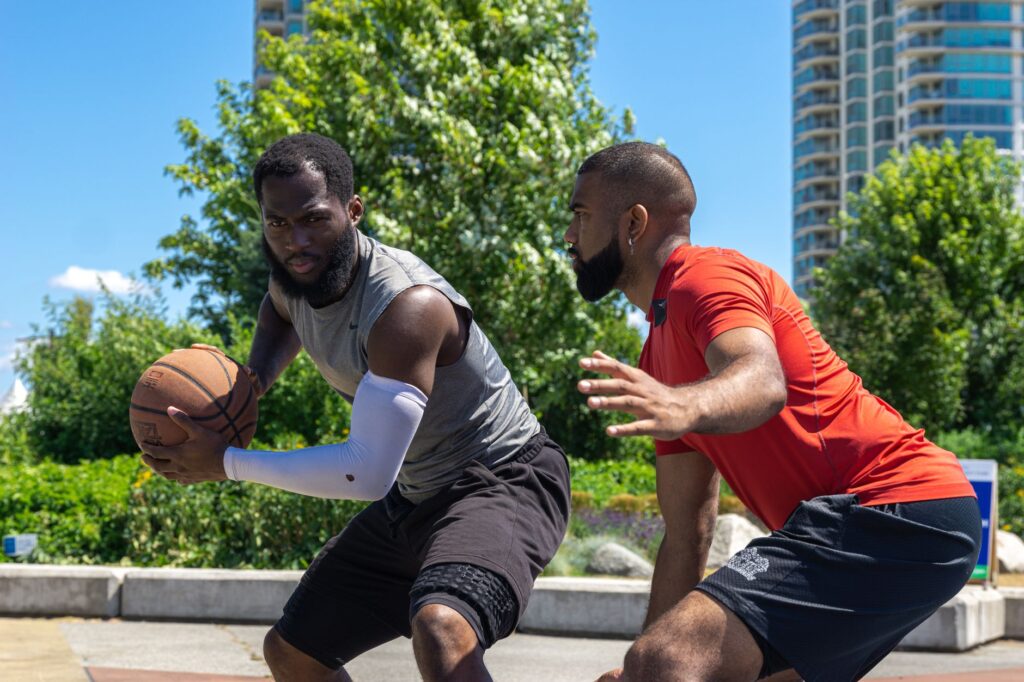 Two men playing a competitive basketball game outdoors on a sunny day.