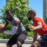 Two men playing a competitive basketball game outdoors on a sunny day.