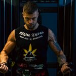Focused man with tattoos works out in a dimly lit gym, showcasing strength and determination.