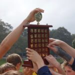 Group of young athletes raising a wooden trophy, symbolizing victory and teamwork.