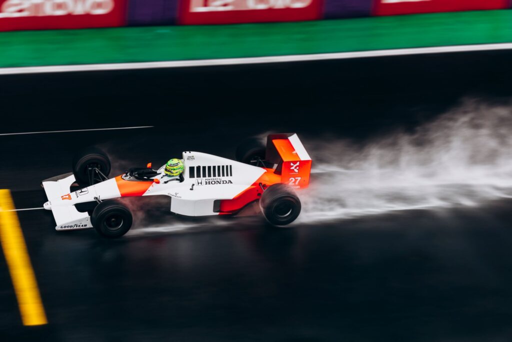 High-speed Formula 1 car races on a wet track, leaving a trail of spray behind.