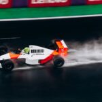 High-speed Formula 1 car races on a wet track, leaving a trail of spray behind.