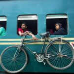 Travelers on a train looking out the window with a bicycle attached, capturing daily life travel.
