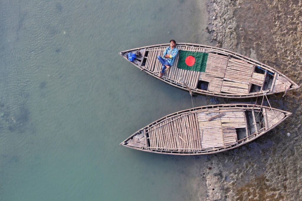 Aerial shot of a wooden boat with the Bangladesh flag on a calm river, showcasing tranquil Bangladeshi life.