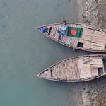 Aerial shot of a wooden boat with the Bangladesh flag on a calm river, showcasing tranquil Bangladeshi life.